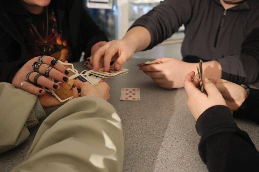 Neljä nuorta pelaa korttia pöydän ääressä.